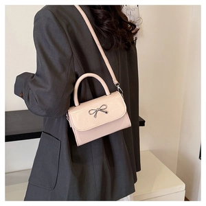 Detail of light beige crossbody bag featuring silver bow ornament and chic metal handle