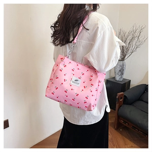 Detail of pink cherry print canvas tote bag with metal chain strap on model shoulder