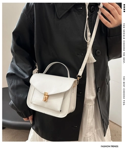 Detail of white mini crossbody bag with gold buckle and top handle on black jacket