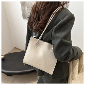 Borsa tote beige trapuntata minimalista indossata da modella con blazer verde scuro