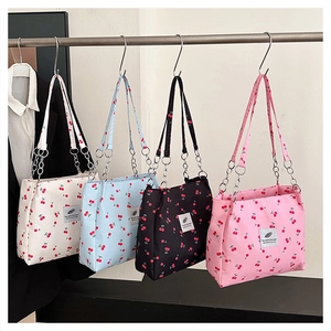 Detailed row of four cherry print tote bags with metal chain straps hanging in a line