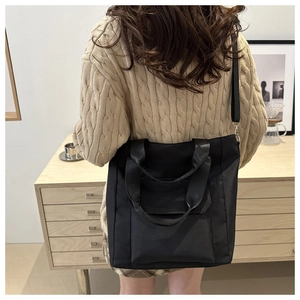 Detail of a large black nylon tote bag with wide handles and adjustable shoulder strap