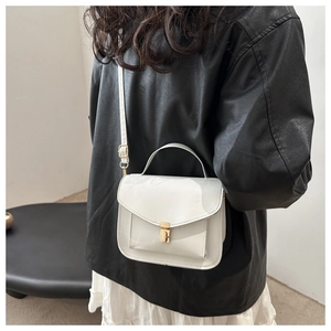Detail of white leather messenger bag featuring a golden lock clasp and top handle