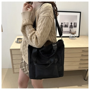 Detail of black nylon tote bag with adjustable strap and front flap pocket on a model