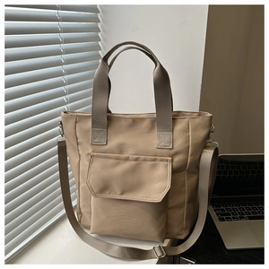 Detailed view of khaki nylon tote bag with front flap pocket on a sunlit office desk