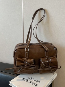 Dark brown retro Boston bag with white stitching and double bow pockets on a desk
