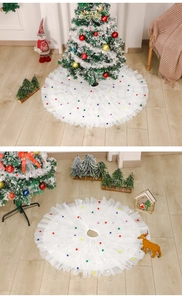 Macro detail of white layered tulle Christmas tree skirt featuring colorful pom-pom edges