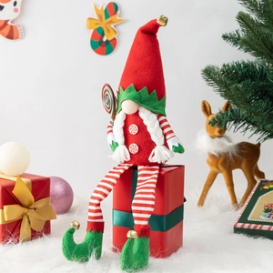 Christmas gnome doll with red bell hat and candy cane sitting on a festive gift box