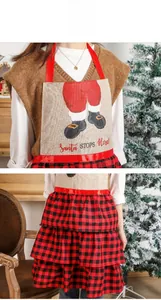Detail of linen Christmas apron with Santa STOPS Here print and red black plaid ruffles