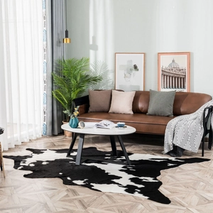 Faux cowhide rug with irregular black and white cow print on wood floor in living room
