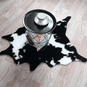 Faux cowhide rug with black and white cow print on light wood floor in modern living room