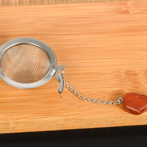 Edelstahl-Teesieb mit herzförmigem rotem Kristallanhänger auf einem Hintergrund aus Holz