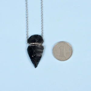 Natural obsidian arrowhead necklace with silver wire wrap and chain on blue background