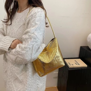 Détail d'un sac cabas doré métallisé avec motif crocodile porté sur un pull en maille