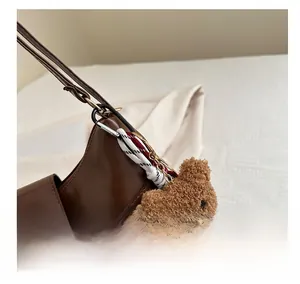 Detail of brown faux leather shoulder bag with a cute plush bear charm accessory