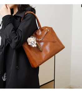 Braune Tragetasche aus glänzendem Leder mit Katzenanhänger und schwarzem Trenchcoat