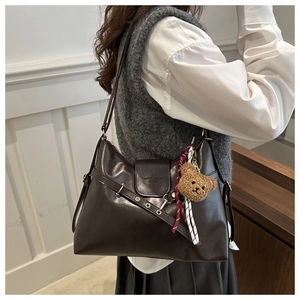 Detail of dark brown tote bag with bear charm and red ribbon decoration from side view