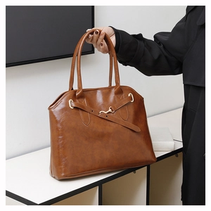 Detail der karamellfarbenen glänzenden Ledertasche mit Metallschnalle und Griffen