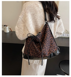 Detail of leopard print tote bag with black leather straps and side bow on knit sweater