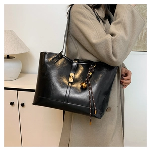 Détail d'un grand sac cabas en cuir noir avec fermoir rotatif et breloque tissée
