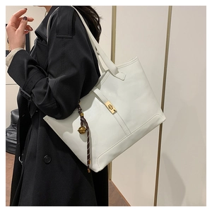 Grand sac cabas blanc avec boucle dorée et pompon, porté par un mannequin