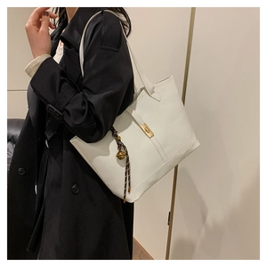 Détail d'un sac cabas blanc avec fermoir en métal doré et breloque tissée