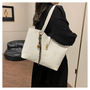 Vue détaillée d'un sac cabas blanc avec fermoir doré et pendentif porté par un mannequin
