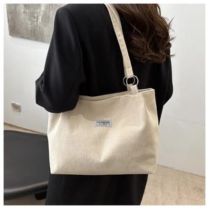 Detail of beige corduroy tote bag featuring metal ring strap connectors and fashion label