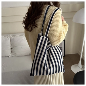 Close-up of blue and white striped canvas tote bag worn by a model in a cozy room