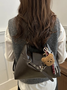 Vintage brown leather tote bag with a cute bear charm, worn as a stylish crossbody bag