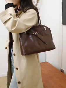 Dunkelbraune Vintage-Tote-Bag aus Leder für Damen, getragen mit einem hellen Pendler-Mantel