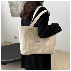 Close-up of beige corduroy tote bag showing soft ribbed texture and fashion label detail