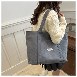 Close-up of grey corduroy tote bag with fashion label shown in a lifestyle setting