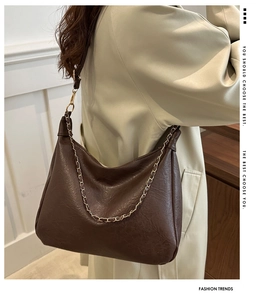 Détail du sac croissant marron foncé avec texture grainée et chaîne dorée sur trench