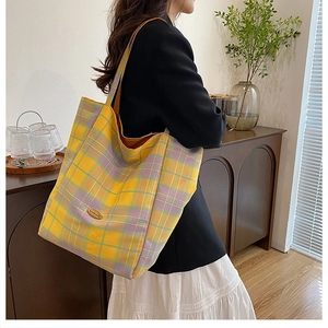 Detail of yellow plaid canvas tote bag with metal logo and reinforced shoulder strap