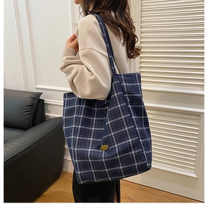 Detail of blue and white plaid canvas tote bag with golden metal logo plaque