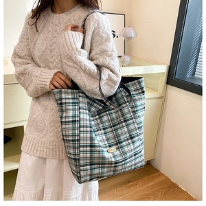 Detail of green plaid canvas tote bag featuring an oval metal handmade brand tag