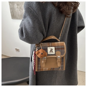 Détail d'un sac à main en laine à carreaux marron avec breloque ours et foulard rayé