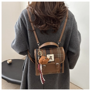 Detail view of vintage plaid backpack featuring a plush bear charm and leather flap