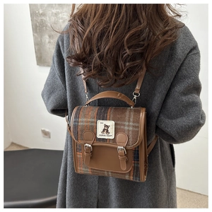 Detail of vintage brown plaid backpack with leather straps and bear patch on gray coat
