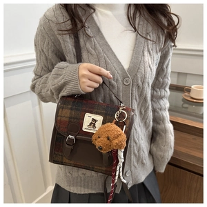 Detail of plaid wool crossbody bag featuring a leather trim and a cute plush dog pendant