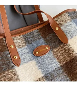 Detail of plaid wool tote with leather logo tag and metallic rivets on brown fabric
