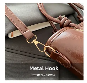 Close-up of golden metal hook and leather knot detail on a vintage brown shoulder bag