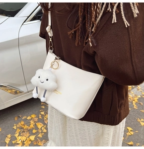 Dettaglio borsa a spalla in pelle bianca con logo dorato e ciondolo a nuvola di peluche