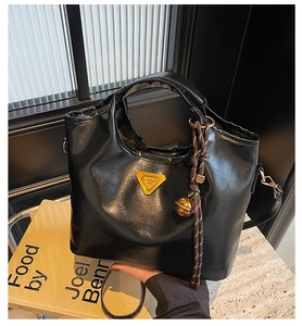Détail d'un sac seau en cuir noir brillant avec logo triangulaire jaune et pendentif