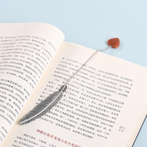 Segnalibro a piuma in metallo argento con ciondolo a cuore in cristallo su un libro