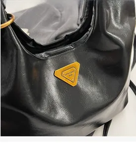Détail du cuir noir brillant avec plaque logo dorée triangulaire et anneau métallique