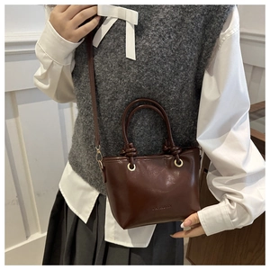 Detail of a brown glossy leather handbag with gold hardware and embossed fashion logo