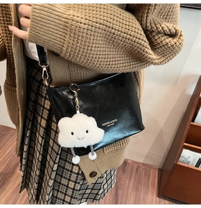 Dettaglio borsa in pelle nera lucida con logo dorato e ciondolo a nuvola in peluche carino
