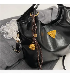 Détail d'un sac seau en cuir noir brillant avec logo triangulaire doré et pompon